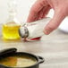 A person holding a Tablecraft flat paneled salt shaker over a bowl of soup.