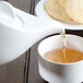 A Villeroy & Boch white porcelain teapot pouring tea into a white cup with cookies.