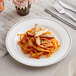 A WNA Comet white plastic plate with silver accent bands holding pasta with meat and sauce with a fork and knife on a napkin.