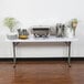 A Lancaster Table & Seating white plastic folding table set up for a buffet with plates and a vase of flowers.