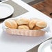 A Tablecraft woven rattan-like bread basket filled with rolls on a table.