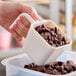 A hand using a white Carlisle portion scoop to pour chocolate chips into a container.