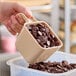 A hand using a Carlisle beige portion scoop to pour chocolate chips into a container.