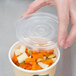 A hand holding a plastic lid over a bowl of food.