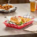 A red rectangular plastic fast food basket with a cheeseburger and fries inside on a table.