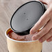 A hand holding a black lid over a container of food.