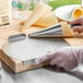 A person using a Waring waffle cone forming tool to cut a waffle cone on a metal board.