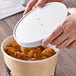 A hand holding a white lid over a bucket of fried chicken.