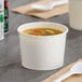 A white double poly-coated paper cup of soup with a white plastic spoon.