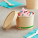 A Kraft paper food cup with ice cream, candy, and a wooden spoon.