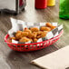 A red oval plastic fast food basket filled with fried chicken nuggets on a table.