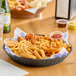 A black plastic diner platter with french fries, onion rings, and a drink on a table.