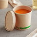 An EcoChoice kraft paper food container with a vented lid filled with soup on a table.