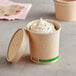 A close-up of a EcoChoice kraft paper food cup filled with ice cream and sprinkles with a vented lid.