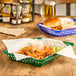 A Forest Green rectangular plastic fast food basket with a burger inside on a table.