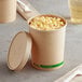 A Kraft paper food cup with macaroni and cheese and a fork on a napkin.