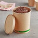 A EcoChoice kraft paper food cup filled with chocolate ice cream and a spoon with a vented lid.