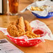 A round red plastic fast food basket filled with fried chicken and french fries.