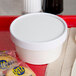 A white Choice paper food container with a lid on a red tray.