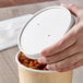 A hand placing a white vented lid on a white Choice soup container full of food.