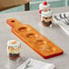A wooden Acopa tasting flight paddle with desserts and spoons on a table.