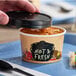 A person holding a Choice double poly-coated paper soup container with a vented paper lid full of hot food.