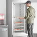 A man standing in front of an unassembled Avantco end load sheet pan rack filled with pastries.