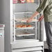 A person putting trays of pastries into an Avantco end load sheet pan rack in a refrigerator.