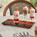 An Acopa walnut finish flight tray with desserts in glasses on a table.