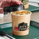 A hand holding a Choice Medley paper soup cup filled with soup.
