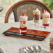 An Acopa walnut finish flight tray with desserts and spoons on a table.