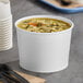 A white Choice paper food cup filled with soup with noodles and vegetables.