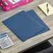 A table with blue Avery folders, a calculator, and papers.