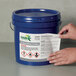 A hand holding a container with an Avery UltraDuty GHS label on it.