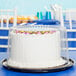 A white cake with flowers on a tray with a clear plastic cover.