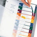 A hand opening a binder with colorful file folders labeled with Avery Ready Index dividers.