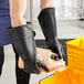 A person wearing Winco black rubber gloves pouring liquid into a container.