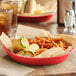 A red round plastic platter holding a sandwich and fries on a table.