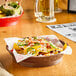 A brown plastic diner platter holding a bowl of nachos with salsa, jalapenos, and cheese on a table.
