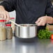 A person cooking in a Vollrath stainless steel sauce pan.