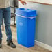 A man in blue jeans putting a plastic bottle in a blue Lavex slim rectangular recycling bin with a blue drop shot lid.