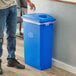 A man standing next to a Lavex blue rectangular recycling can with a blue lid with holes.