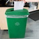 A woman's hand putting paper into a green Lavex recycling bin with a slot lid.