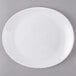 A white Arcoroc Zenix glass steak plate with a white rim on a gray surface.