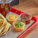 A clear plastic container filled with brown Carnival King Jalapeno Cheese Sauce on a tray of food.