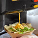 A person pouring Carnival King jalapeno cheese sauce onto a bowl of nachos.