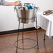 A person pouring drinks into a Tablecraft brushed stainless steel beverage tub on a table with a white tablecloth.
