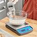 A person pouring flour into a bowl on an AvaWeigh compact digital portion scale.