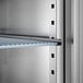 A close-up view of an adjustable metal shelf inside a stainless steel reach-in refrigerator.