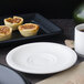 A white porcelain saucer with a cup of coffee and food on a table.